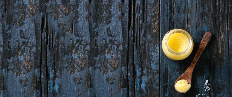A golden jar of traditional A2 Bilona Cow Ghee next to an indigenous Indian cow.